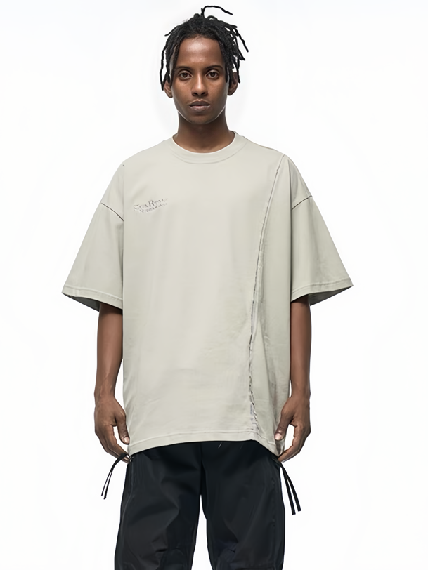 Model wearing an oversized beige asymmetric stitch tee with deconstructed seam detail and wide black pants