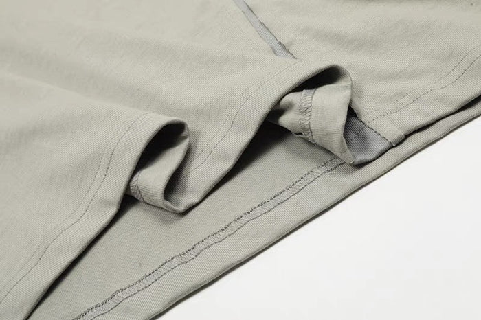 Close-up of a light gray cotton tee hem with exposed seams, asymmetric stitching, and folded sleeve detail