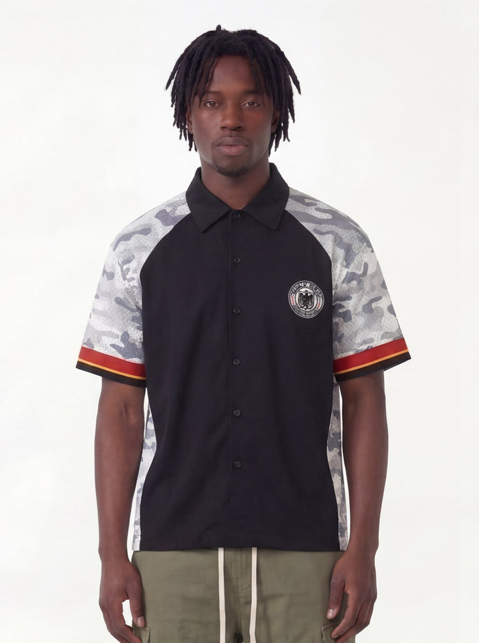 Black streetwear button-up shirt with gray camo sleeves and a circular eagle patch, worn by a male model
