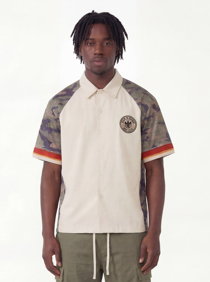 Cream button-up shirt with camo raglan sleeves, eagle patch, and olive drawstring cargo pants on model