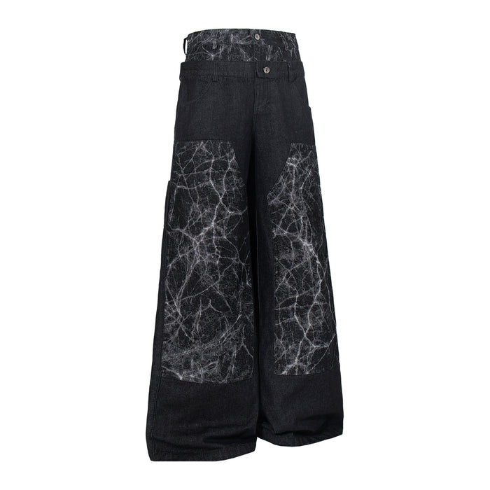 Angled front view of black wide-leg denim pants with cracked panel accents and button fly