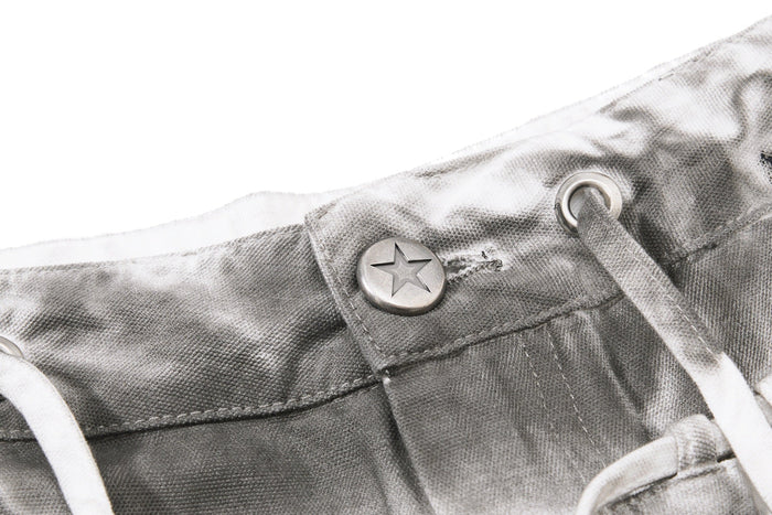 Close-up of waistband button with star engraving and white drawstring on gray denim