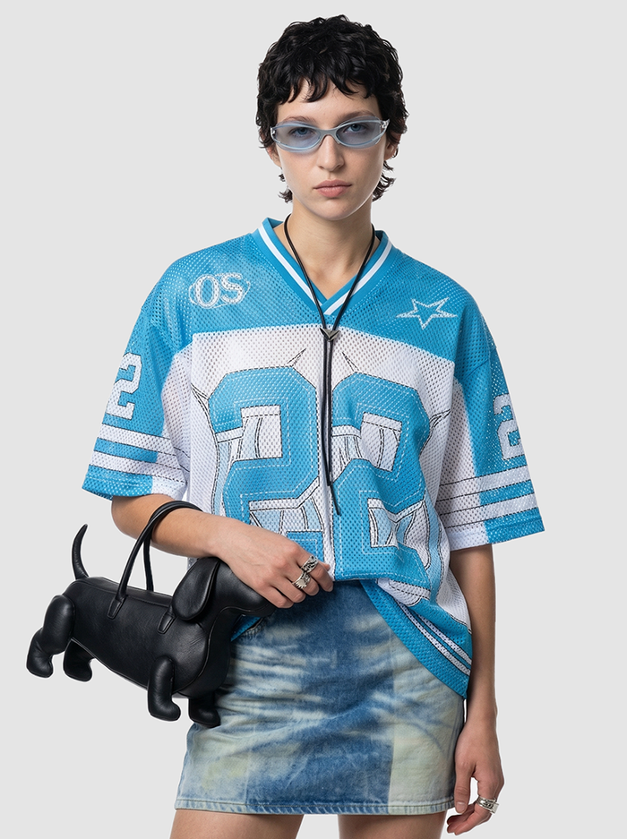 Model wearing a blue and white mesh jersey T-shirt with number 22, paired with a denim mini skirt and black dog-shaped handbag