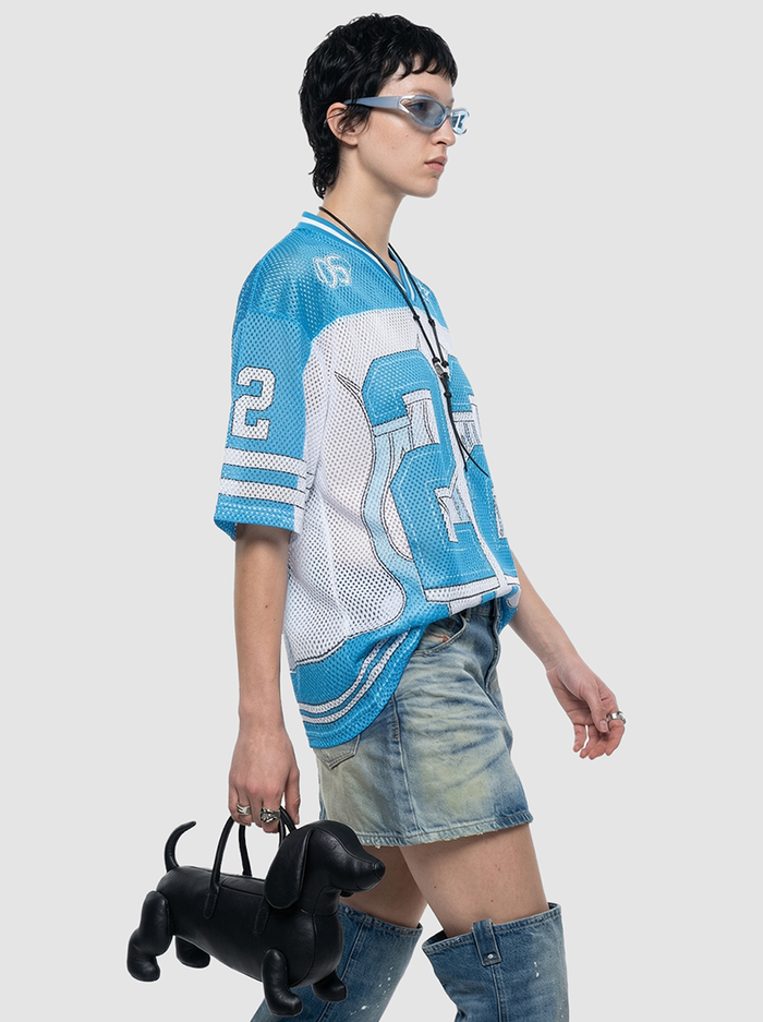 Model wearing a blue and white mesh jersey with number 22, styled with denim skirt, boots, and a black dog-shaped bag