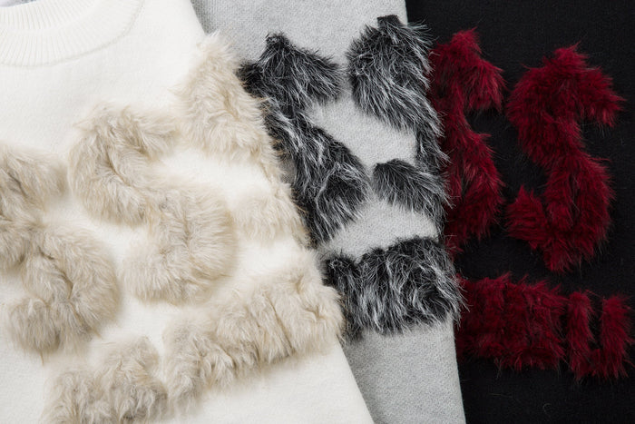 Close-up of faux-fur lettering in cream, black, and burgundy on knit sweater