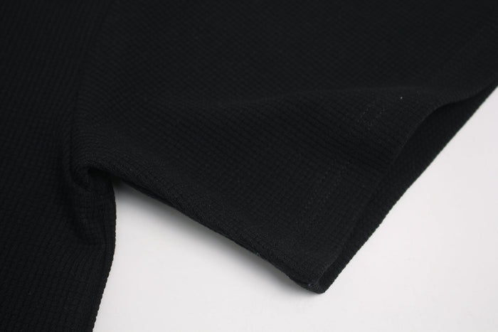 Black ribbed streetwear T-shirt fabric close-up with folded sleeve and hem on a white background