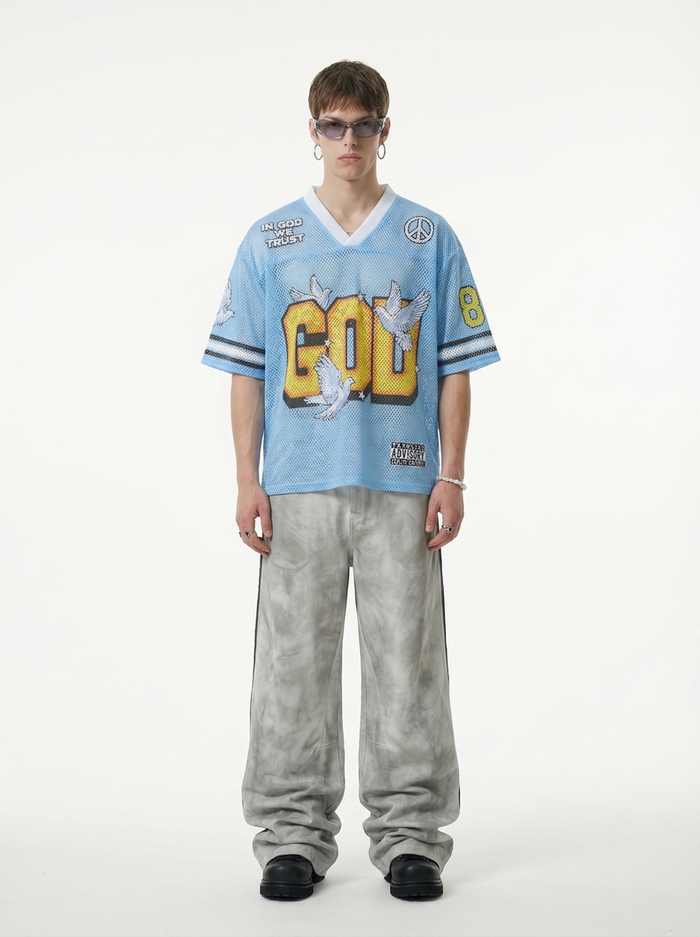 Model wearing a light blue mesh jersey T-shirt with bold GOD graphic, doves, and streetwear details