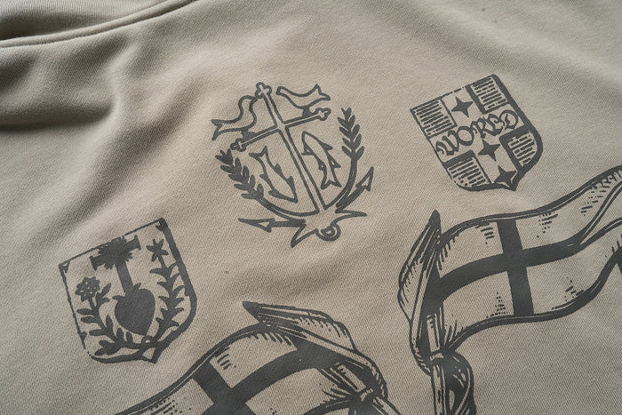 Close-up of back graphics on taupe hoodie, including crest emblems and flag prints