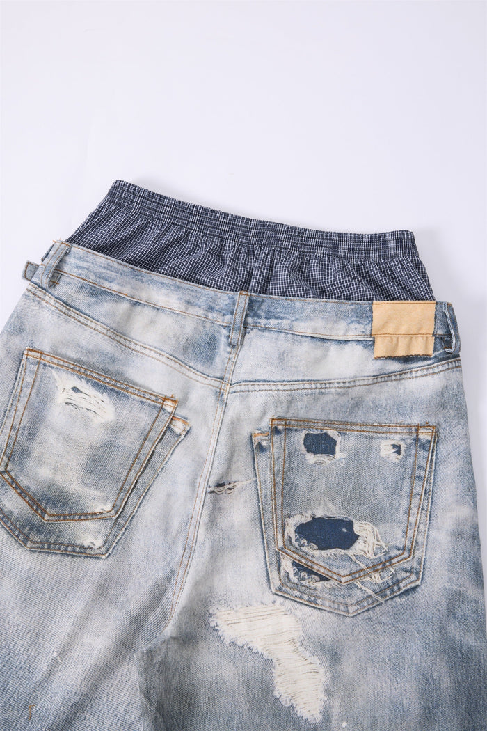 Back waist close-up of light wash distressed jeans with plaid waistband and tan patch detail