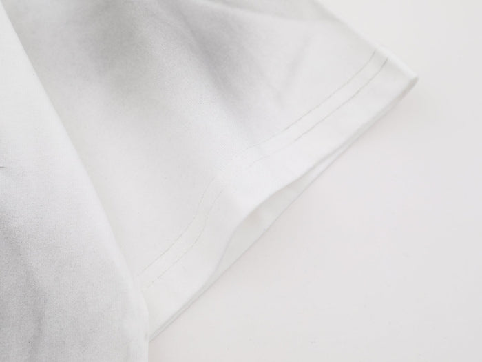 Close-up of a white washed graphic tee sleeve with soft cloud-dye texture and visible hem stitching