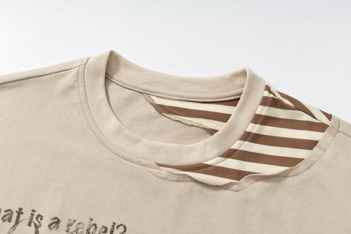 Beige layered graphic tee with striped faux collar and distressed streetwear print in close-up