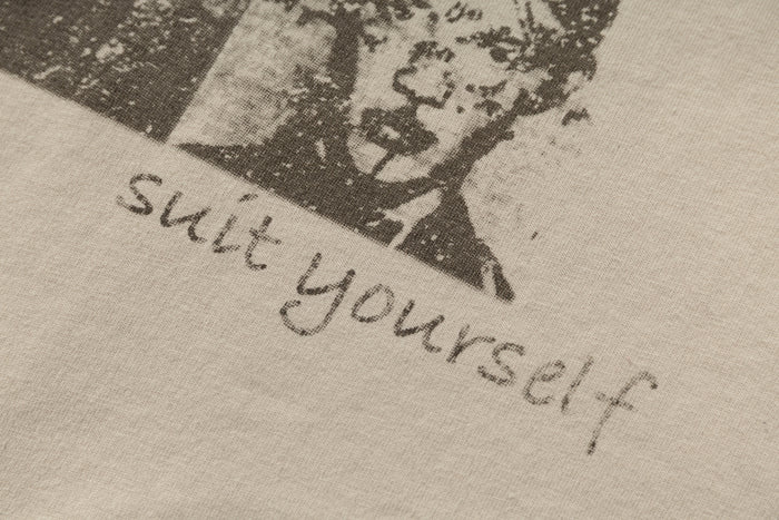 Close-up of a beige streetwear tee with a distressed black portrait graphic and handwritten No Comment text