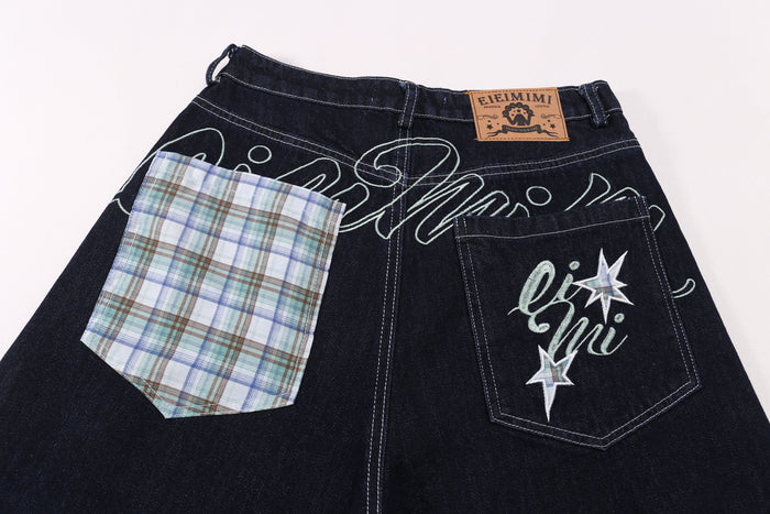 Dark denim shorts with patchwork panels, embroidered script, star accents, and tan waist label