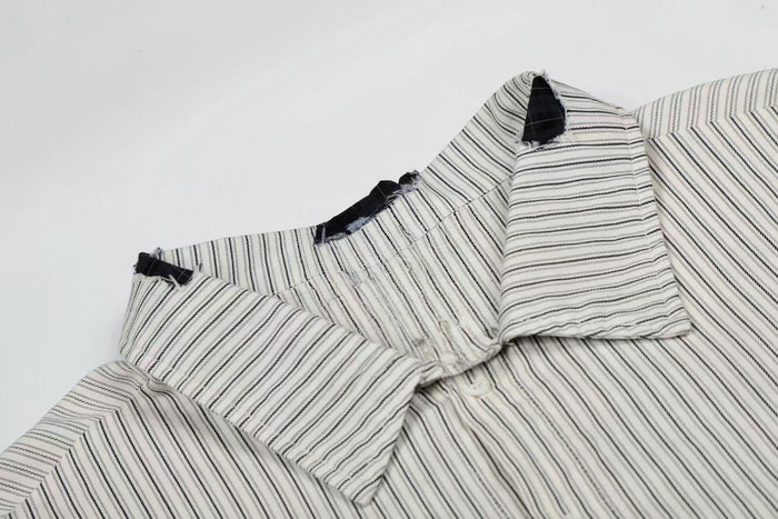 White pinstripe button-up shirt with black patch details and distressed seams, styled as a streetwear graphic top