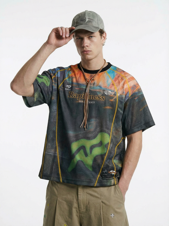 Model wearing a colorful mesh racing jersey tee with graphic print, cap, and relaxed streetwear styling