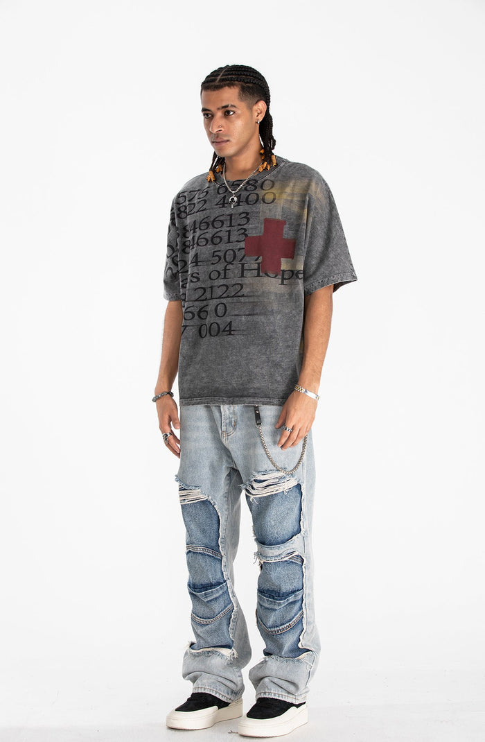 Model wearing a vintage wash oversized graphic tee with red cross print and distressed patchwork jeans on a white background