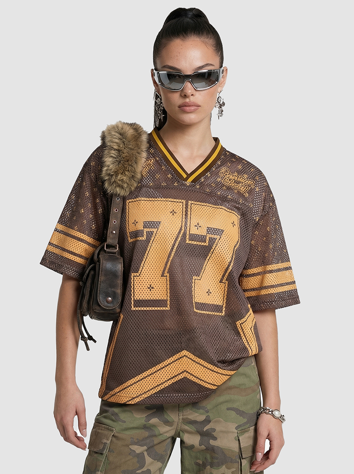 Brown mesh jersey T-shirt with gold 77 graphic and striped trim, styled on a model with camo pants and sunglasses