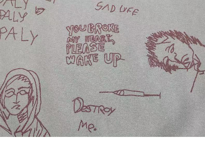 Close-up of light gray sweatshirt front graphic with handwritten text and sketched faces