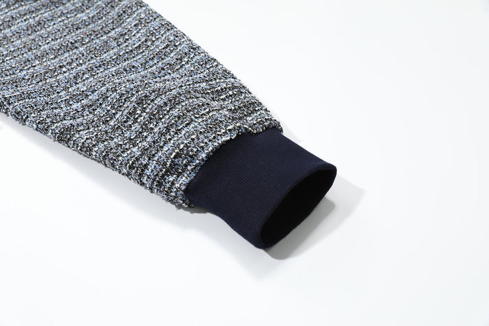 Close-up of a sleeve cuff with dark ribbed trim and speckled boucle knit fabric