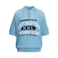 Light blue knit polo shirt with varsity-style text graphic and short sleeves on a white background
