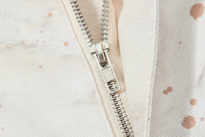 Close-up of the front zipper on cream denim jeans with splatter print