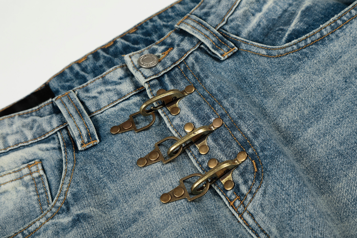 Close-up of front waistband on light wash denim pants with three brass hook closures