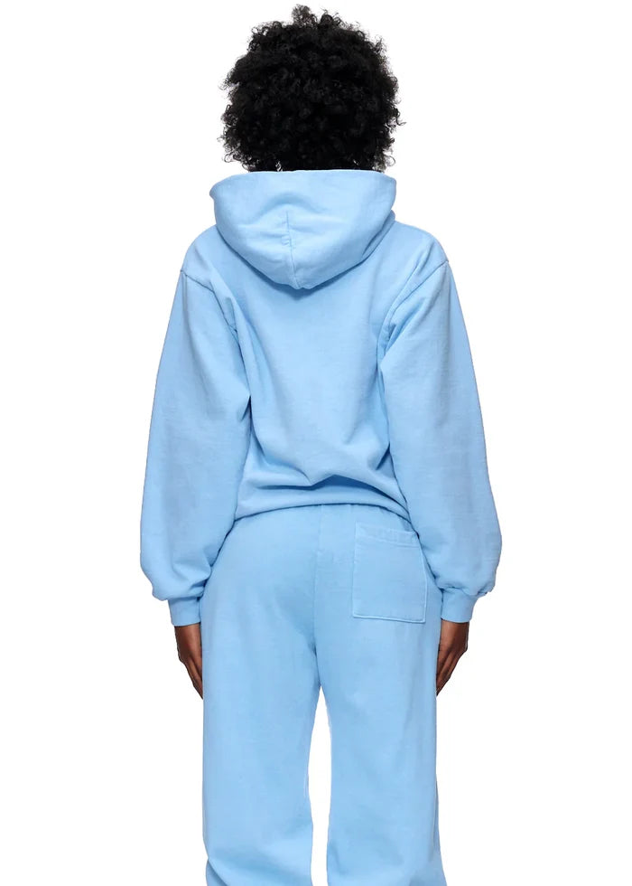 A person stands with their back to the camera, wearing a Sp5der Hoodie – Sky Blue 440GSM Heavyweight Chenille Logo Spider-Web Streetwear Pullover and matching sweatpants, hood up and arms at their sides for a classic streetwear vibe.