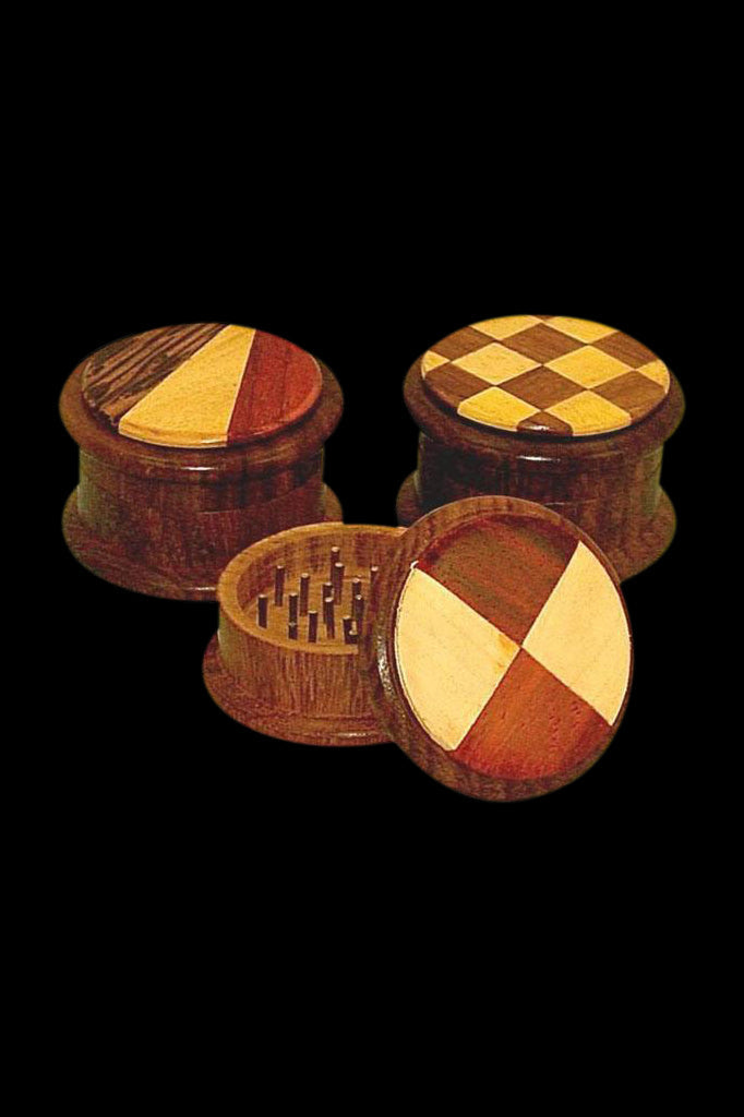 Four wooden cannabis grinders with inlaid geometric patterns on a black background.