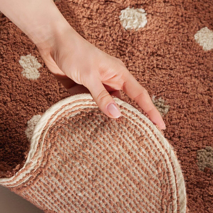 Hand holding a circular rug with a brown and beige patterned rug in the background