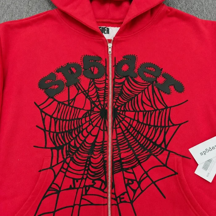 The Sp5der Red Zip-Up Hoodie Black Spiderweb Studded Logo features a bold black spiderweb and "sp5der" lettering on the front, plus a signature white tag on the zipper—making it a standout streetwear essential.