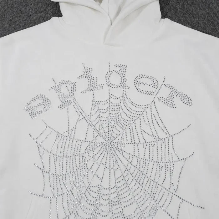 The Sp5der White Rhinestone Spiderweb Crystal Logo Hoodie is a streetwear pullover featuring "Spider" and a large crystal spiderweb design on the front, both made with shiny rhinestones.