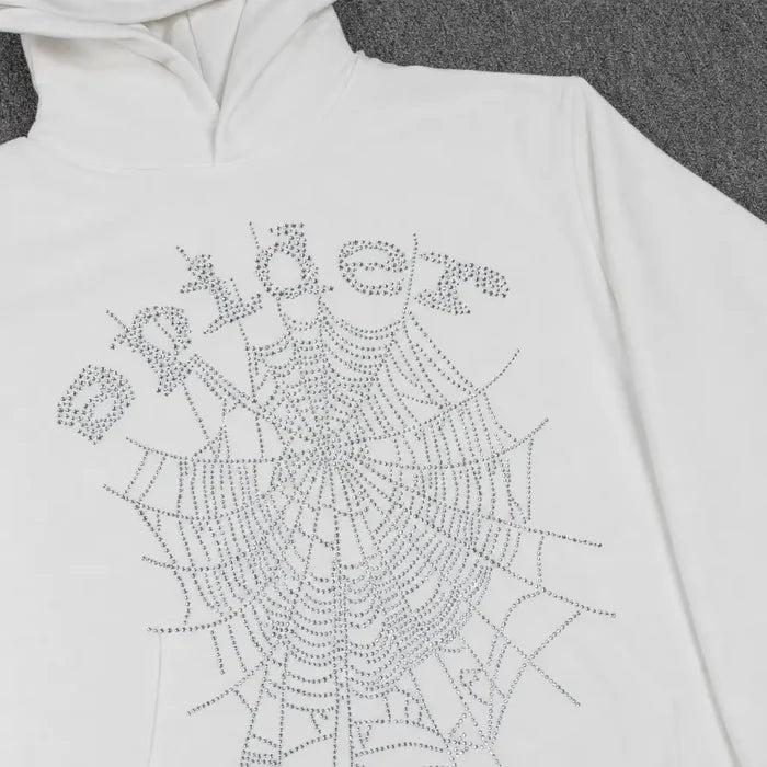 The Sp5der White Rhinestone Spiderweb Crystal Logo Hoodie features a crystal spiderweb and "spider" logo in rhinestones, laid flat on a gray surface—a bold choice for standout streetwear.