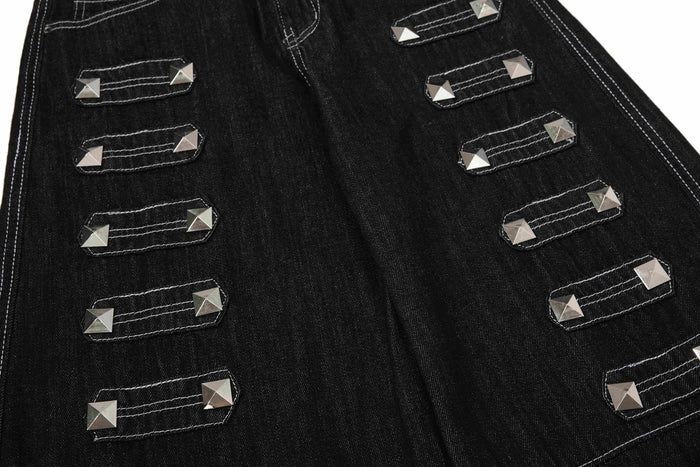 Close-up of black denim pant legs with rows of silver studded strap accents