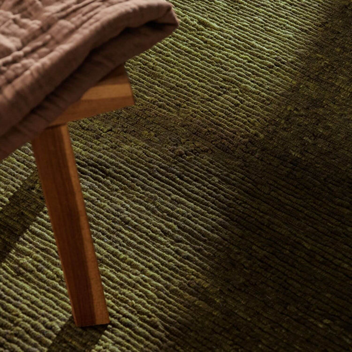 Brown textured rug with a wooden stool partially visible