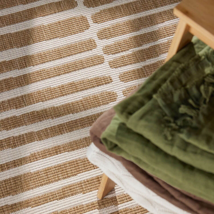 Close-up of a striped rug with a wooden stool and green fabric.