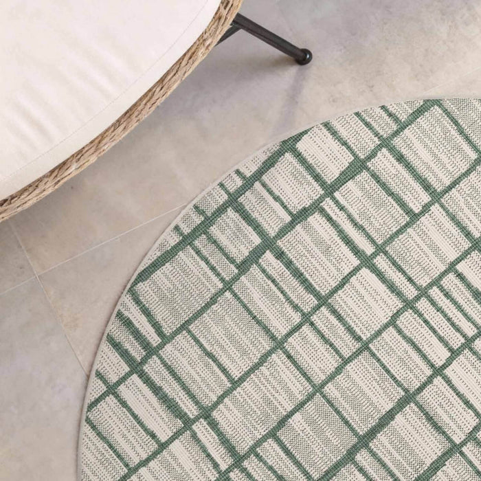 Round green and white checkered rug on a tiled floor with a wicker chair.