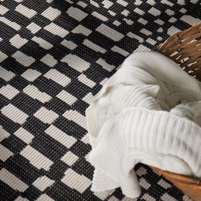 Black and white checkered rug with a woven basket and white fabric on top