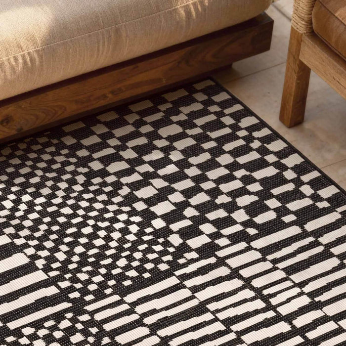 Black and white geometric patterned rug on a wooden floor with furniture.
