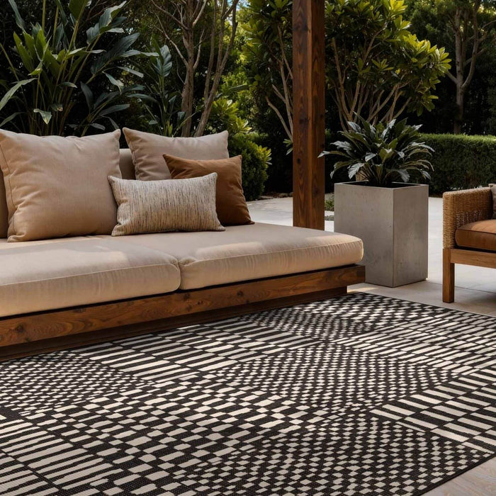 Outdoor seating area with a patterned rug, cushions, and plants.