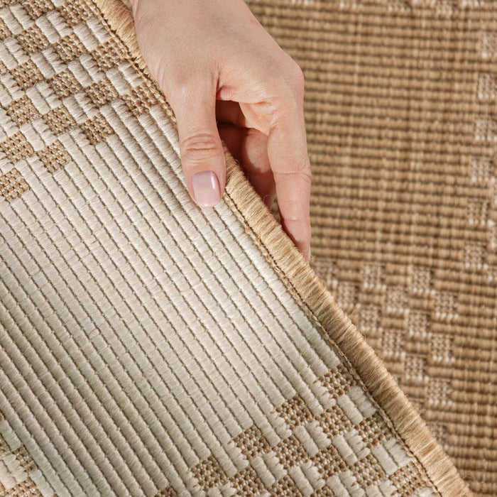 Close-up of a hand touching a textured beige and brown rug.