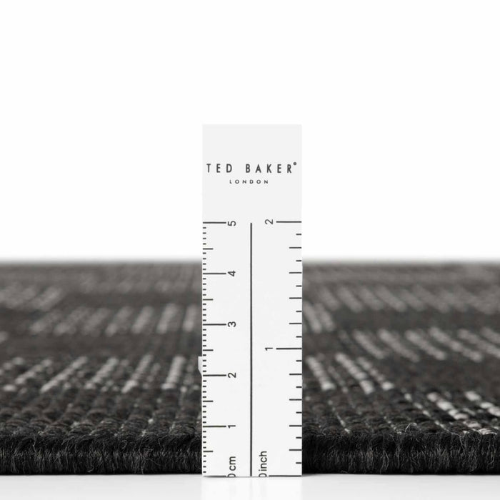 Black textured rug with a ruler for scale on a white background, featuring the Ted Baker London brand.