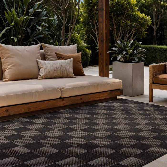 Outdoor seating area with a beige sofa, cushions, and a patterned rug.