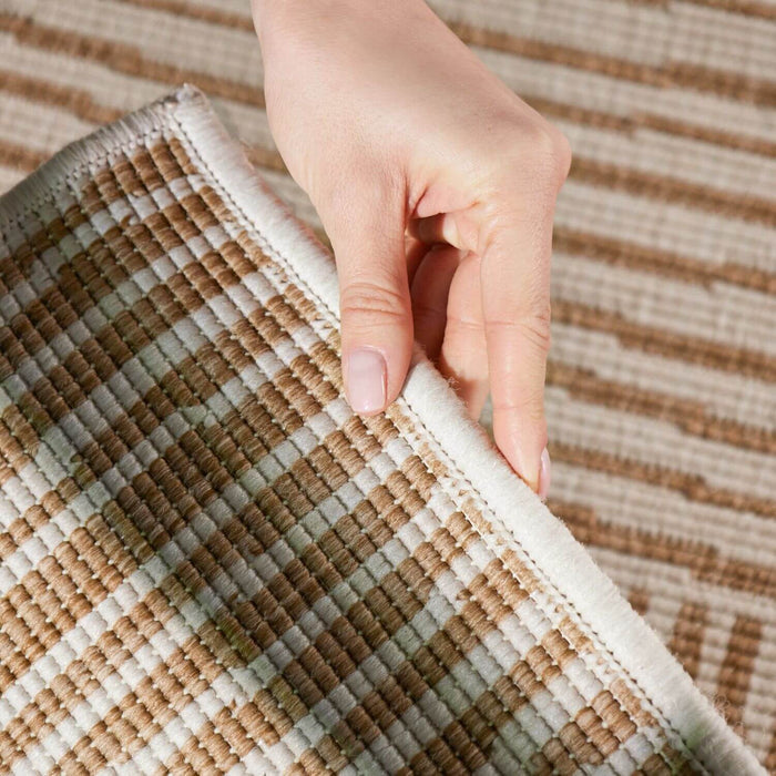 Hand holding a corner of a textured brown and beige rug
