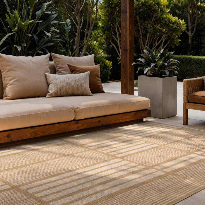 Outdoor seating area with a beige sofa and cushions on a patterned rug, surrounded by greenery.