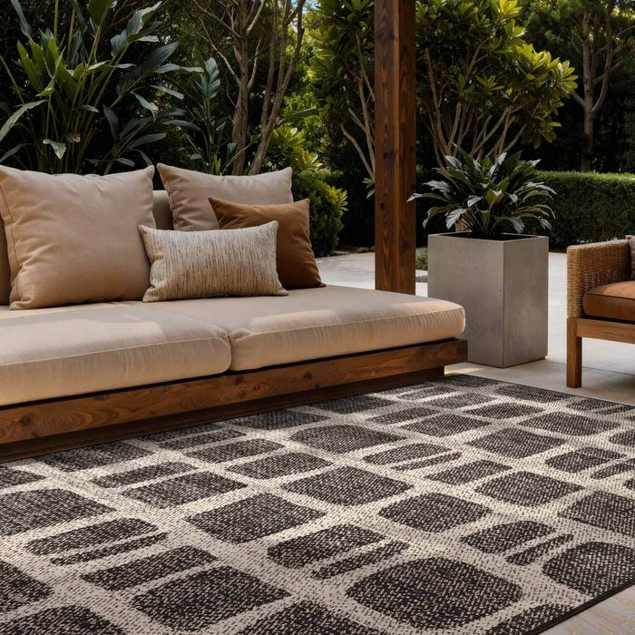 Outdoor seating area with a patterned rug, cushions, and plants.