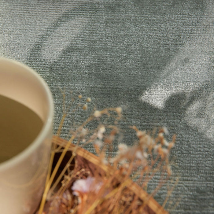 White mug with a beverage and dried flowers on a textured green surface