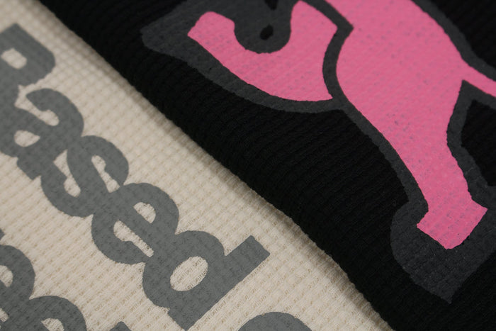 Close-up of waffle-knit fabric with bold pink and gray vintage newspaper-style graphic print on black and cream fabric