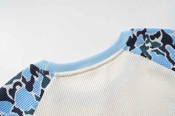 Close-up of light blue ribbed neckline and blue camo shoulder panel on cream raglan long sleeve tee