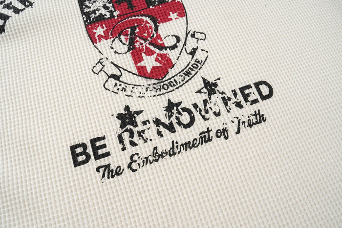 Close-up of lower front print on cream tee showing distressed black text and red crest emblem