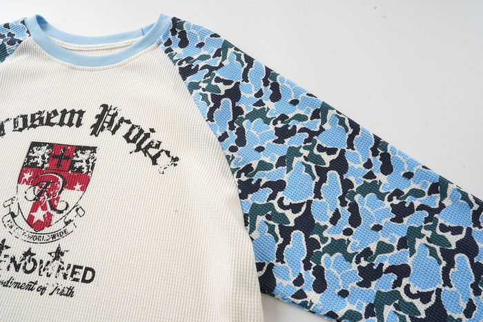 Three-quarter front view of cream raglan long sleeve tee with blue camo sleeves and streetwear crest graphic